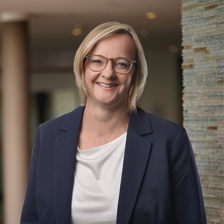 Petra Birk, in elegantem Business-Outfit, lächelt in modernem Hotelambiente