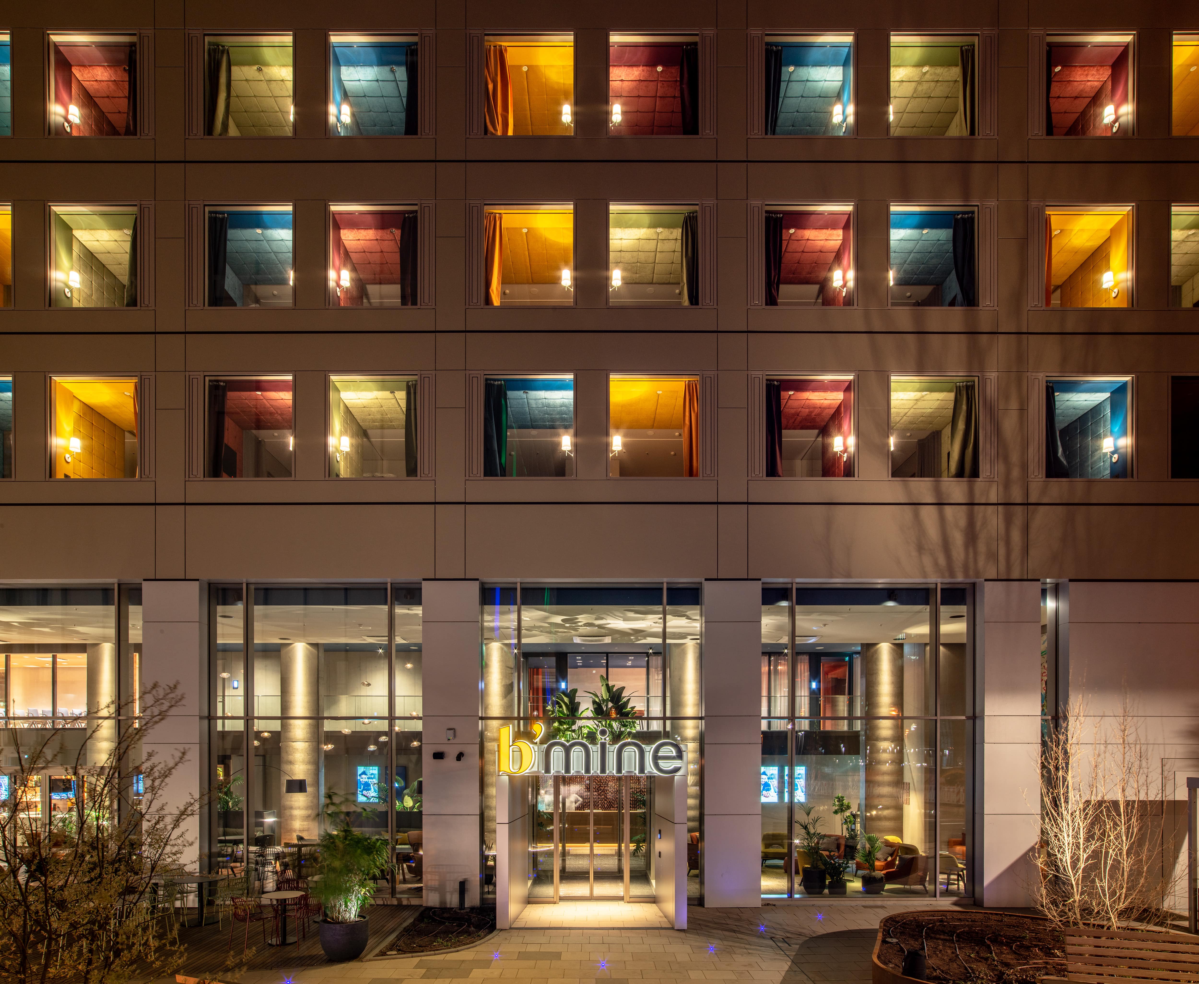 Moderne Hotel-Fassade bei Nacht mit warm beleuchteten Zimmern und einladendem Eingangsbereich