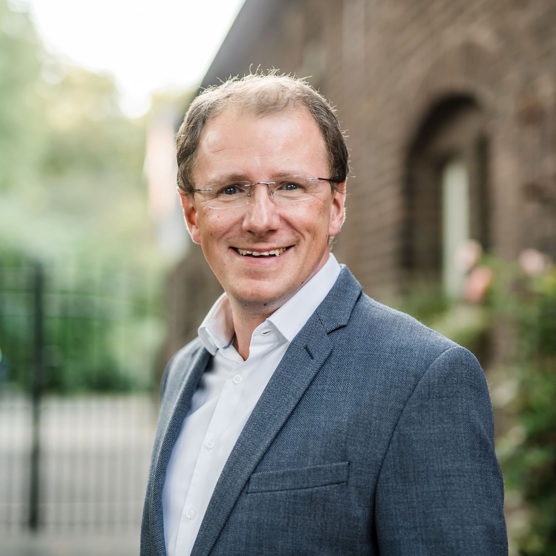Peter Gebhardt, Geschäftsführer von Best Western, in einem stilvollen blauen Sakko, lächelnd vor einer charmanten Backsteinfassade mit grünem Garten im Hintergrund. Sein freundliches Auftreten spiegelt seine Erfahrung und Leidenschaft für die Hotellerie wider
