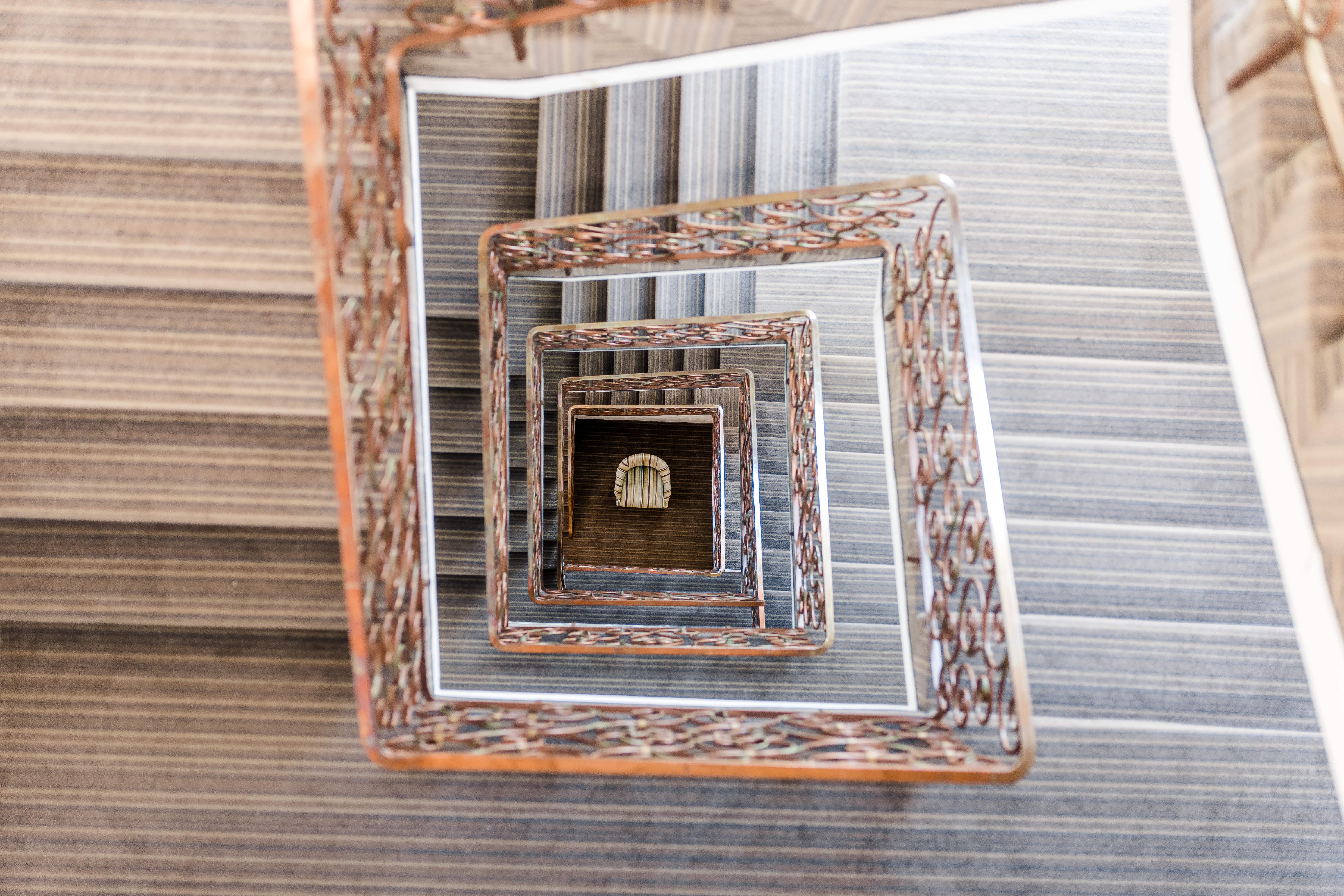 Elegante Treppenperspektive – Architektur mit Charakter Blick von oben in ein kunstvoll verziertes Treppenhaus mit wiederkehrenden, rechteckigen Rahmen, die eine faszinierende Tiefenwirkung erzeugen. Ein harmonisches Zusammenspiel aus klassischen Details und modernem Design